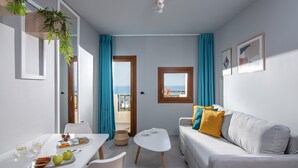 A compact living space with a dining table, a sofa, and a view of the sea through a window. - Villa Elite by Checkin (Hersonissos)