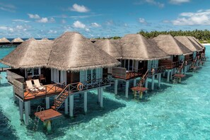 Overwater bungalows with thatched roofs, wooden walkways, and clear turquoise water.