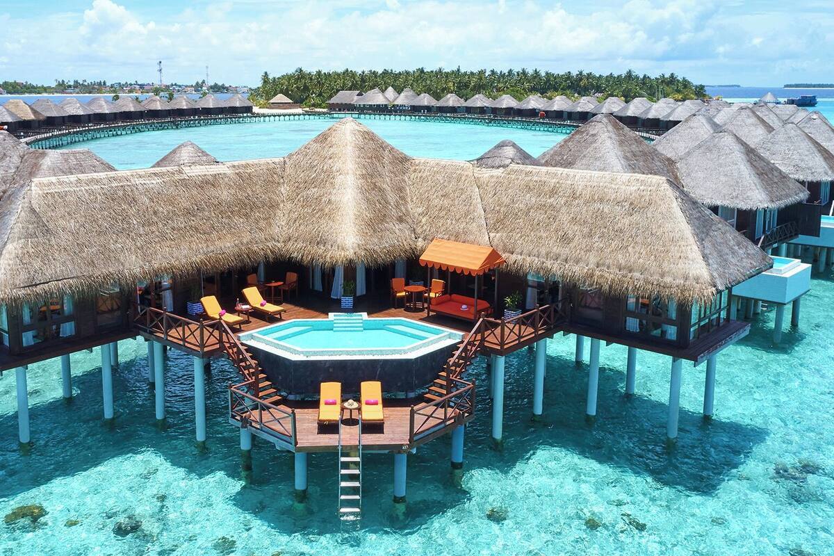 Wasserbungalows mit Strohdächern, ein zentraler Pool und Blick auf den Ozean sowie Palmen.