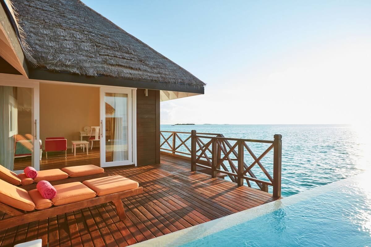 Eine Wasserbungalow-Villa mit Holzterrasse, Liegestühlen und einer Glastür, die zu einem privaten Bereich führt.