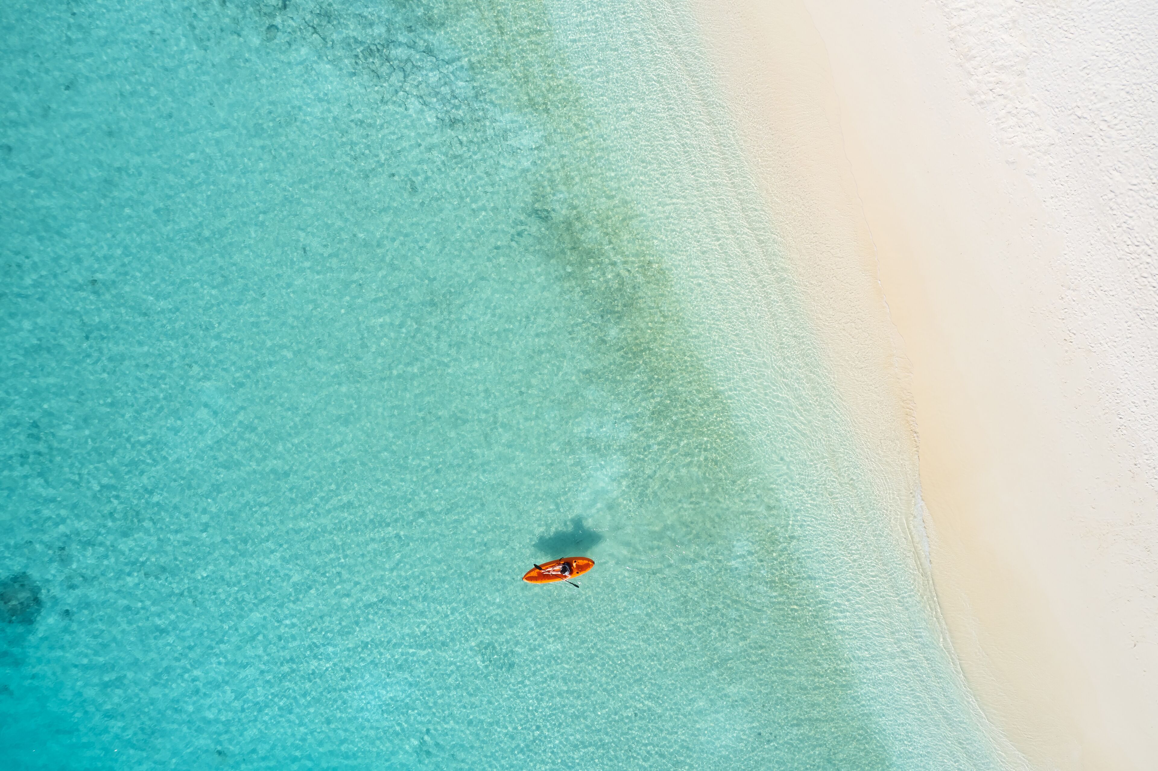 Ein Luftbild zeigt einen Strand mit klarem türkisblauem Wasser und einem Sandufer.