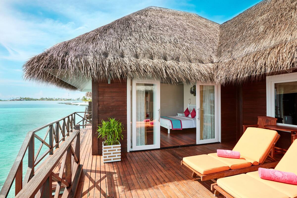 Eine Holzterrasse mit einem Reetdach, einem Bett und zwei Loungesesseln.