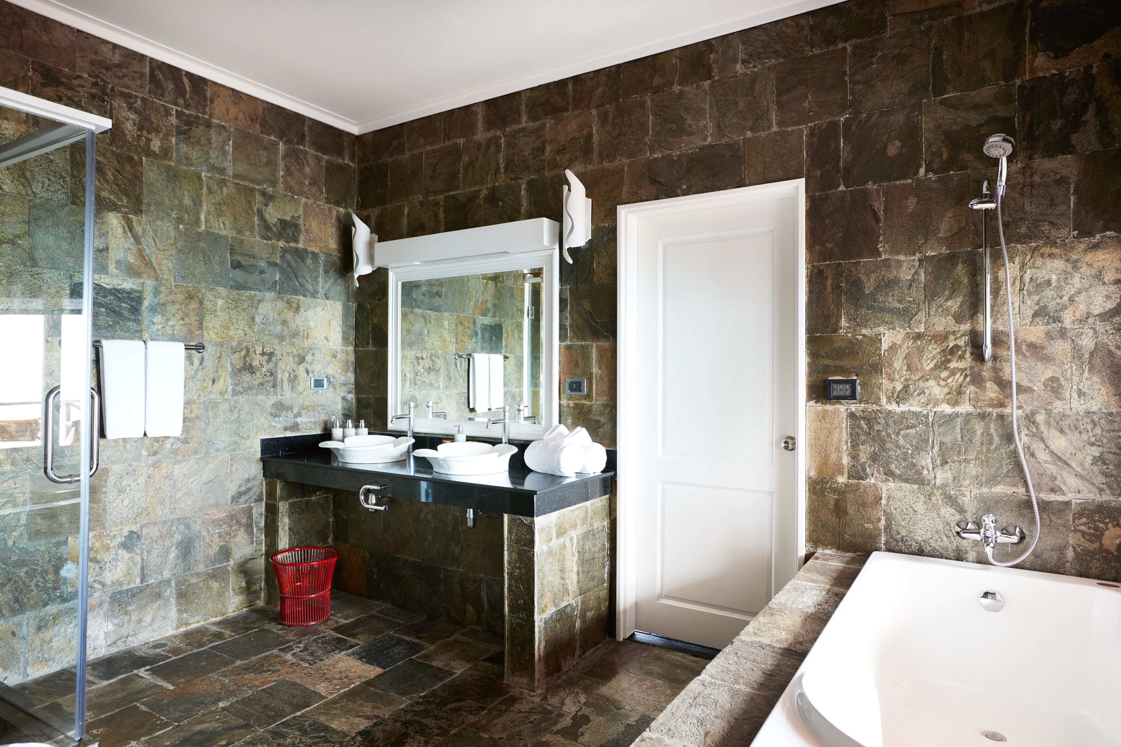 A bathroom with a stone wall, a bathtub, a shower, and a sink with a mirror.