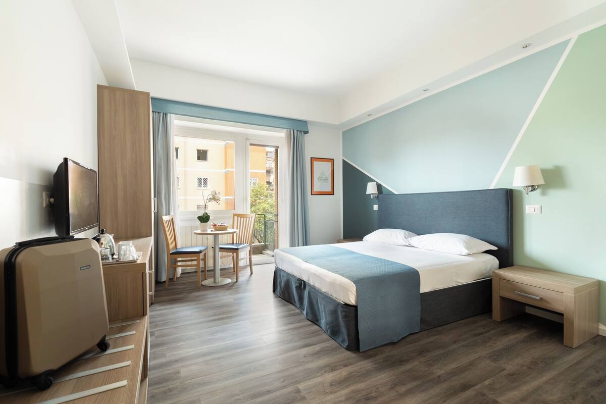 Una habitación de hotel con cama, mesita de noche, televisor y escritorio con silla.