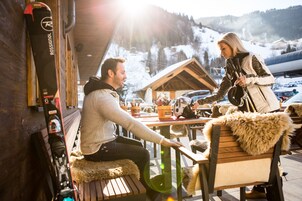 A wooden bench with a fur throw, a ski rack, and a view of a snowy mountain in the background.