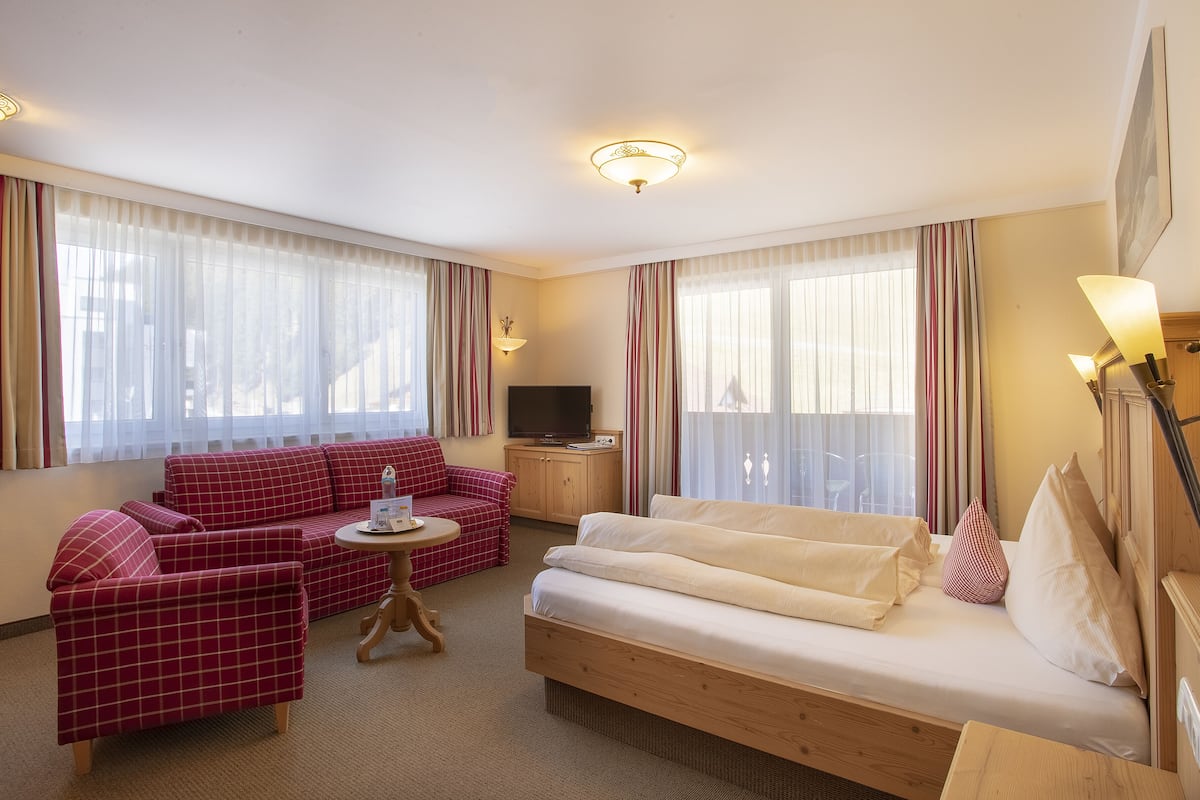 Una habitación de hotel con un sofá rojo a cuadros, un sofá blanco, una mesita de noche de madera, un televisor y una lámpara de pared.