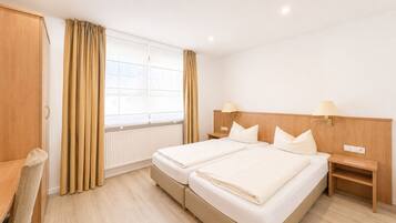 A hotel room with two beds, a desk, and a chair.