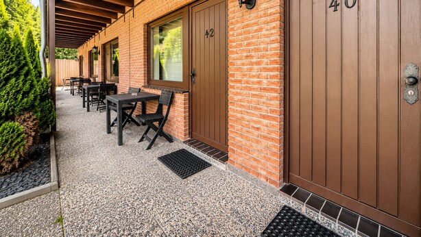 A covered patio with outdoor seating, brick walls, and wooden doors marked with numbers. - Kaiserhof (Lehrte)