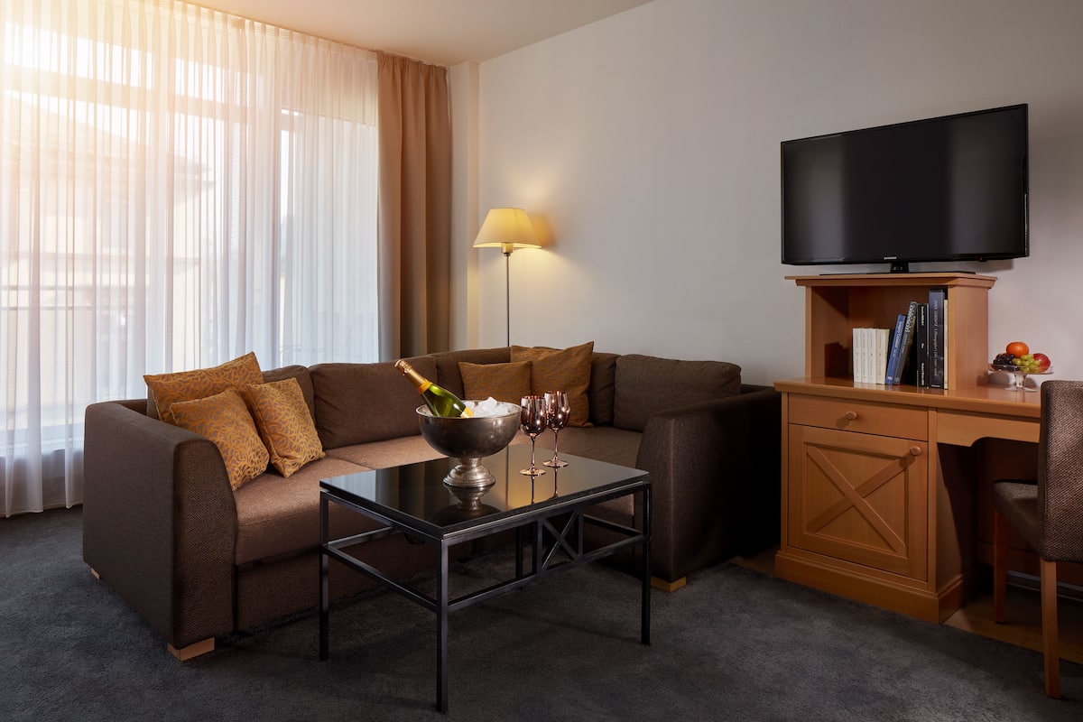 A modern living room with a brown sofa, a glass coffee table, a flat-screen TV, a wooden desk, and a lamp.