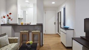 Une cuisine moderne avec des meubles blancs, un plan de travail en bois et un saladier bleu. On y trouve également un coin repas avec un canapé à motifs et une table basse sur laquelle sont disposés des fruits.