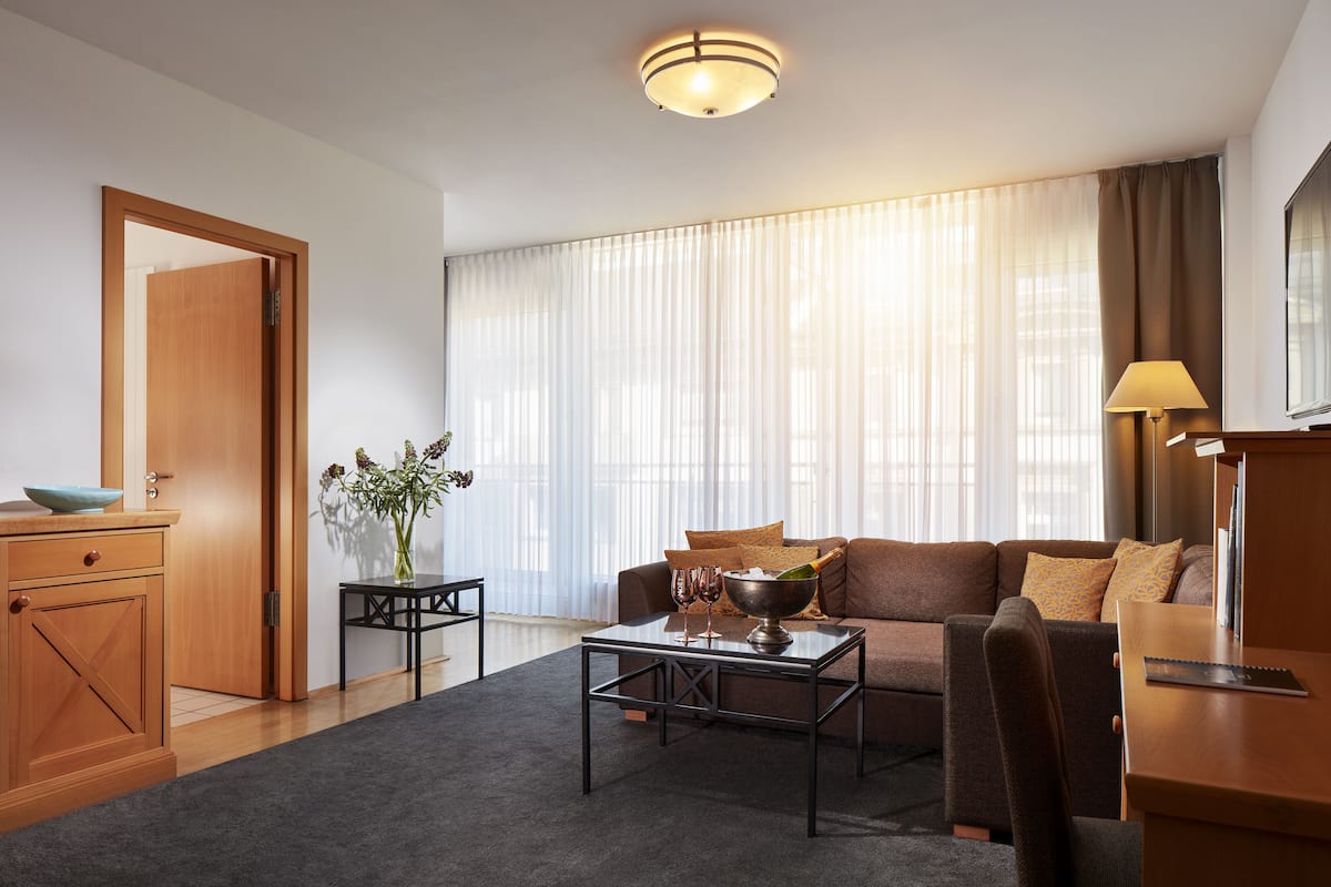 A modern living room with a sofa, coffee table, and a TV. There is a wooden door and a small table with a vase.