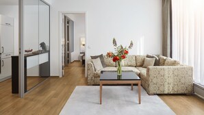 Un salon moderne avec un canapé, une table basse ornée d’un vase de fleurs et un coin cuisine visible à travers une porte vitrée.