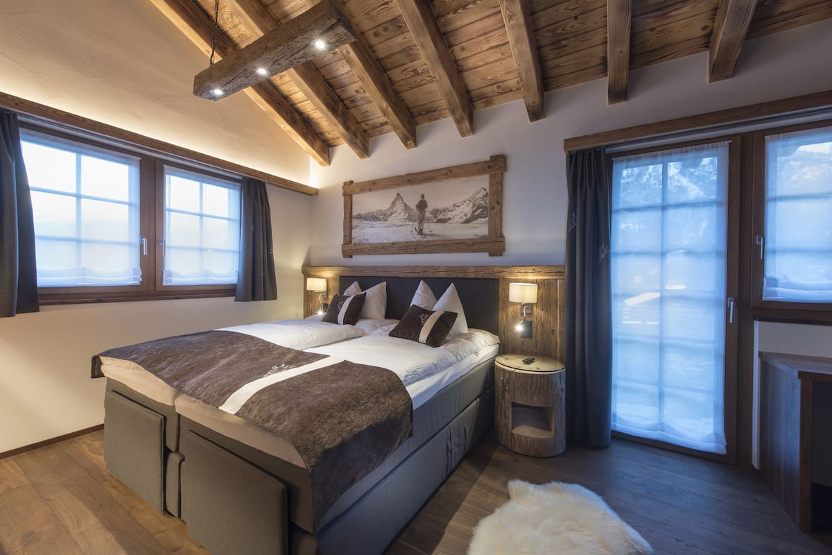 Ein Schlafzimmer mit einem großen Bett, Holzbalkendecke, einem Bild über dem Bett und Blick durch ein Fenster.