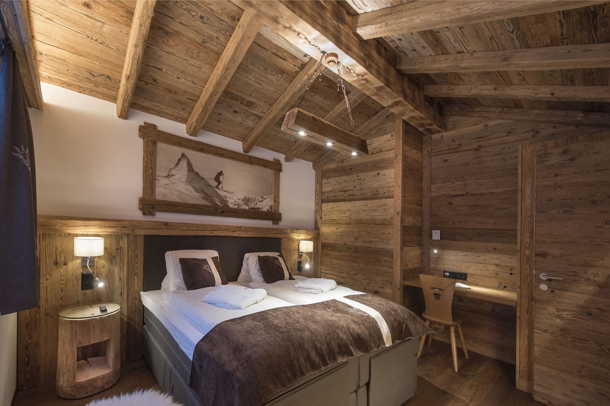 Ein Schlafzimmer einer Holzhütte mit einem Bett, Nachttischlampen, einem Schreibtisch und einem Stuhl.