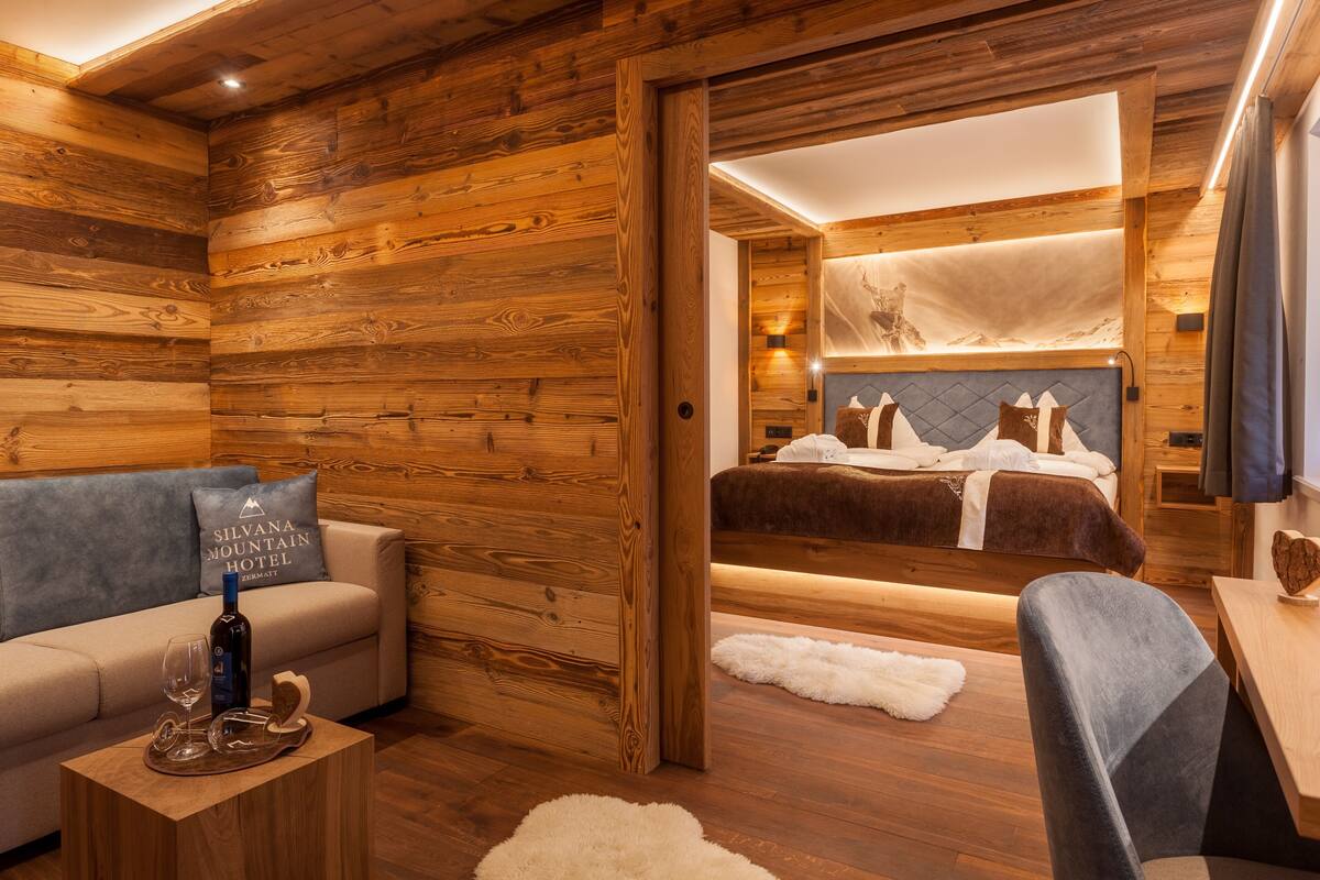 Ein Zimmer mit Holzvertäfelung, einem Bett, einer Couch und einem kleinen Tisch mit einer Flasche und Gläsern.