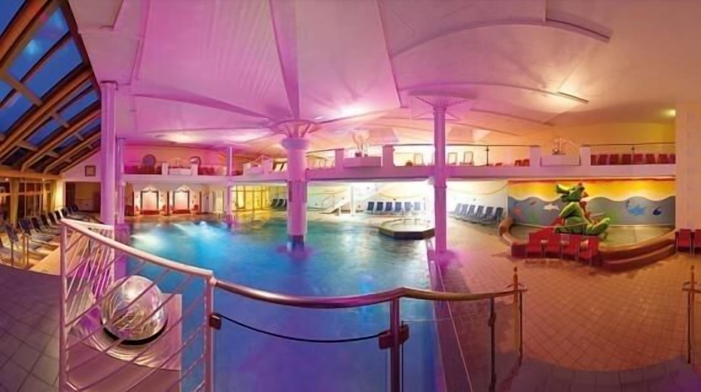Una amplia piscina cubierta con barrera de cristal, varios niveles con balcones y un mural en la pared.