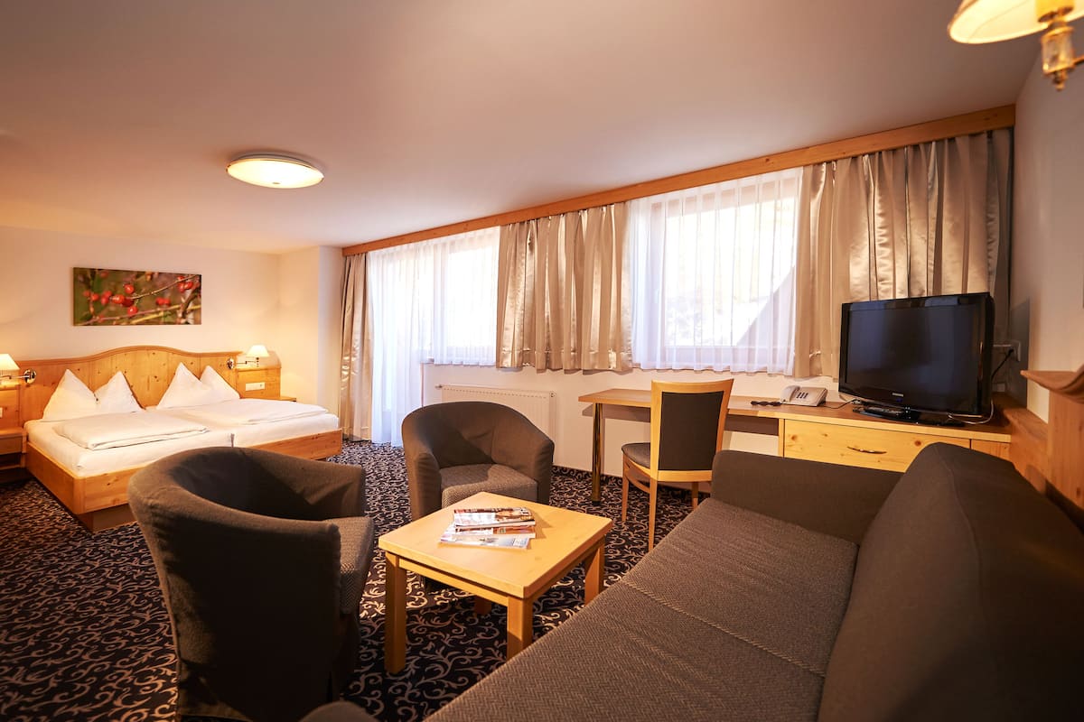 Habitación de hotel con cama, sofá, escritorio con computadora, televisión y una silla.