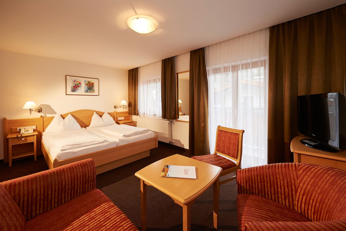 Habitación de hotel con cama, dos mesitas de noche con lámparas, un televisor, una pequeña mesa con una revista y dos sillones.