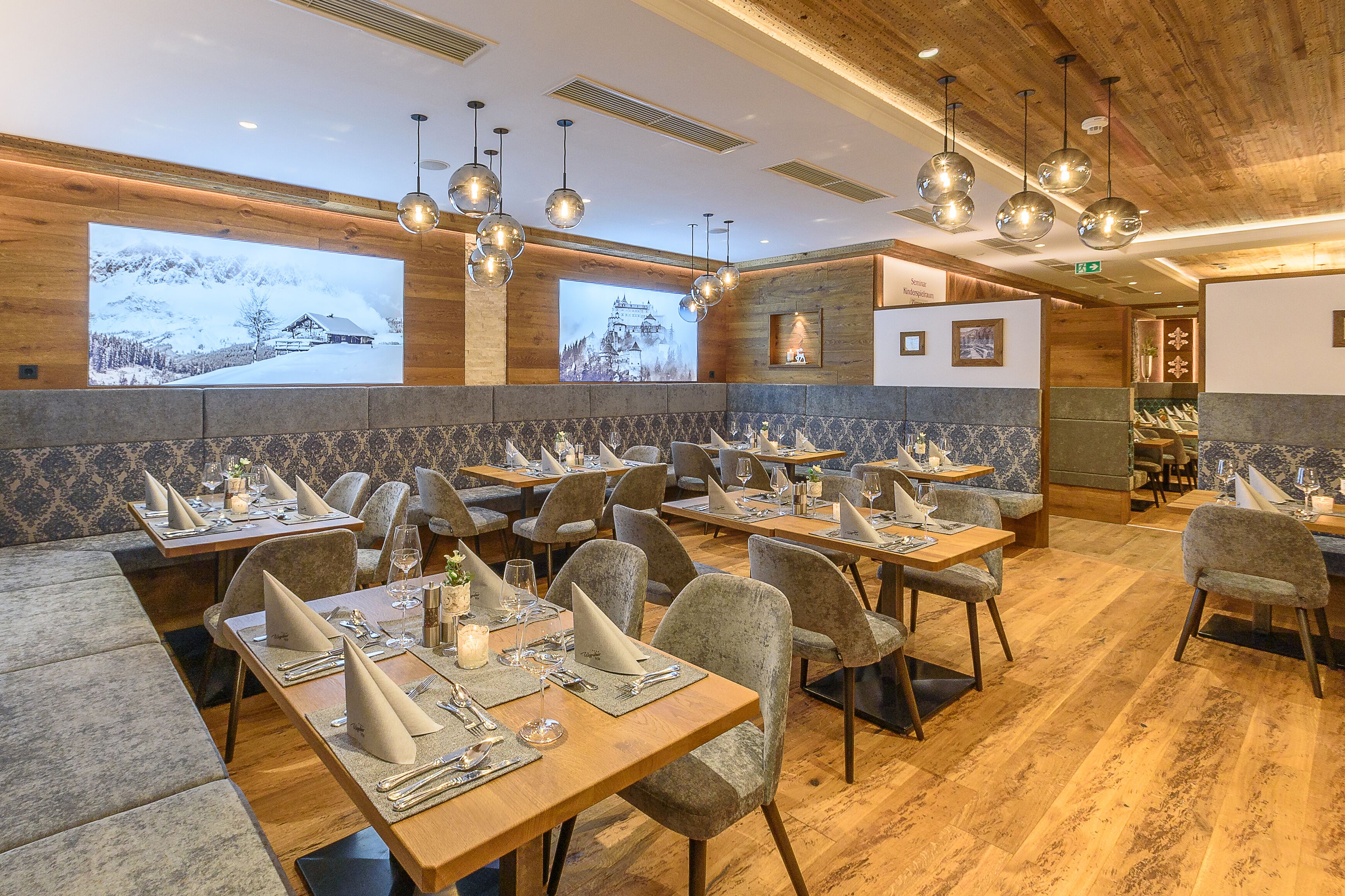 Un restaurant amb parets de fusta, diverses taules de dinar amb cadires i lluminàries esfèriques penjants.