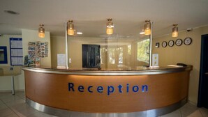 A reception desk with a 'Reception' sign, a bulletin board with notices, and a clock on the wall. - Aquamarine Hotel (Nessebar)