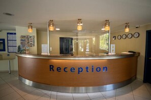A reception desk with a 'Reception' sign, a bulletin board with notices, and a clock on the wall. - Aquamarine Hotel (Nessebar)