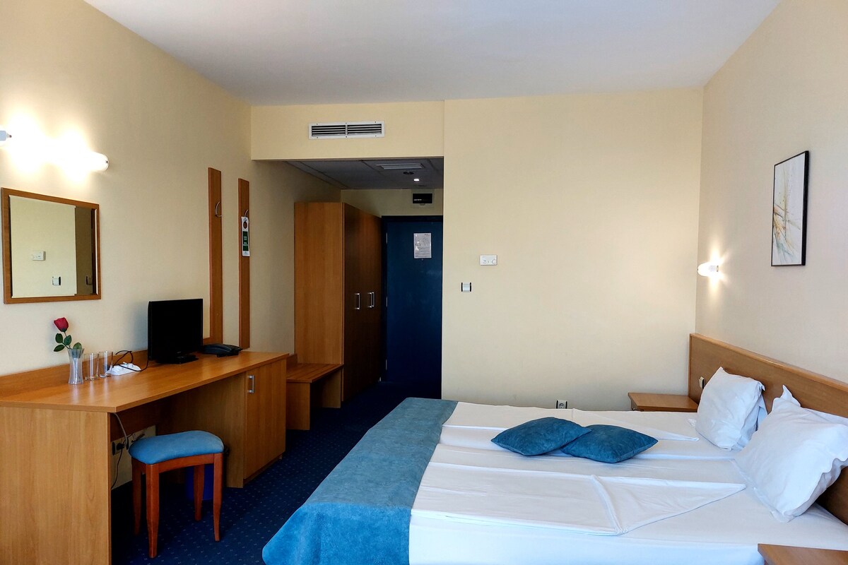 A hotel room with a bed, desk, chair, and a mirror.