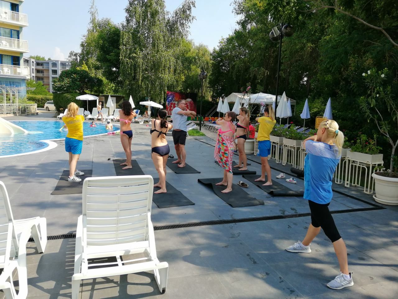 Un grupo de personas haciendo ejercicio sobre colchonetas junto a una piscina.