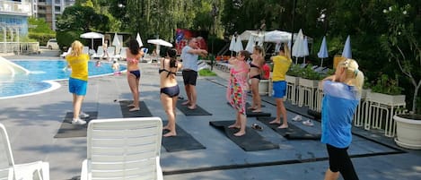 Un grupo de personas haciendo ejercicio sobre colchonetas junto a una piscina.