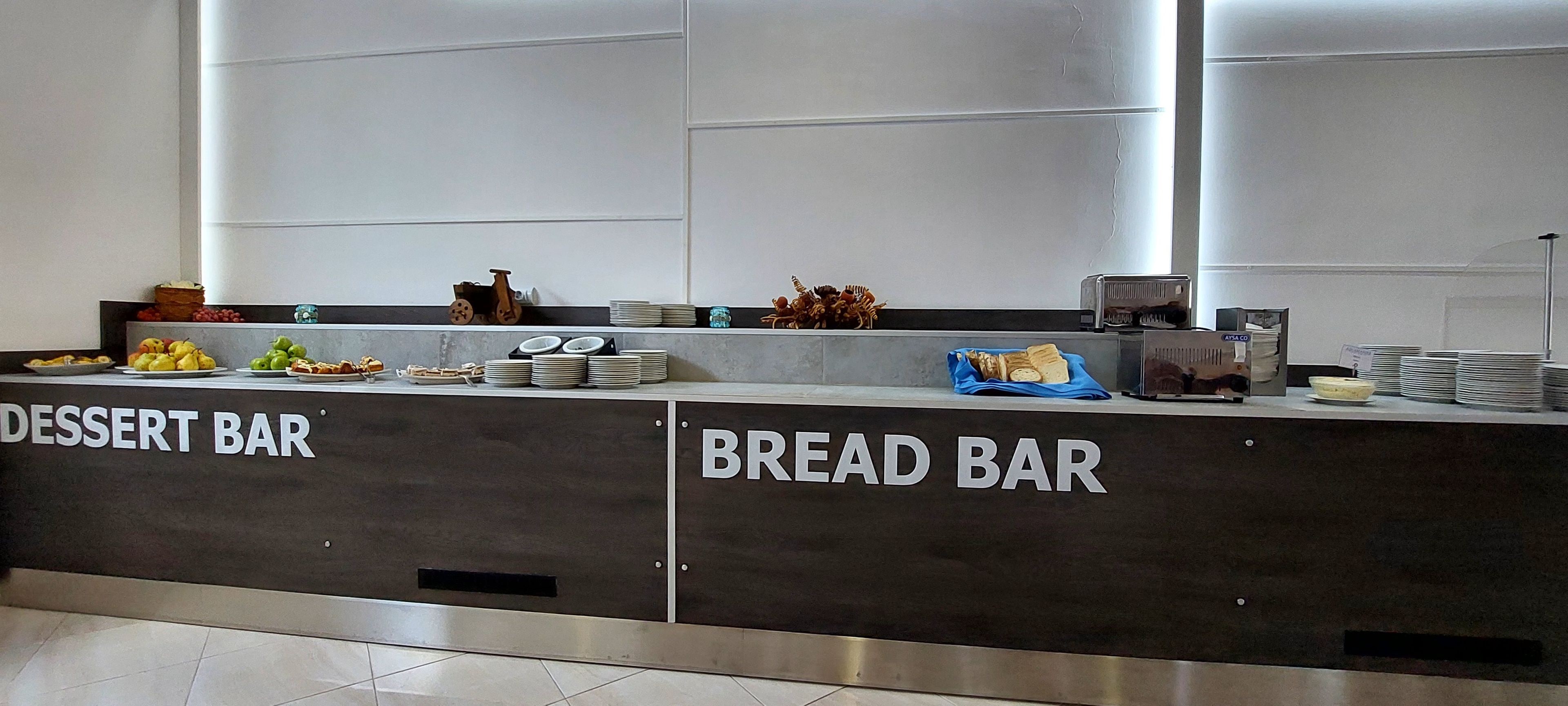 A buffet setup with labeled sections for dessert and bread bars, featuring various food items and utensils.