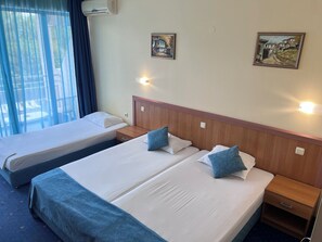 A hotel room with two beds, a wooden headboard, bedside tables, wall-mounted lights, and two paintings. - Aquamarine Hotel (Nessebar)