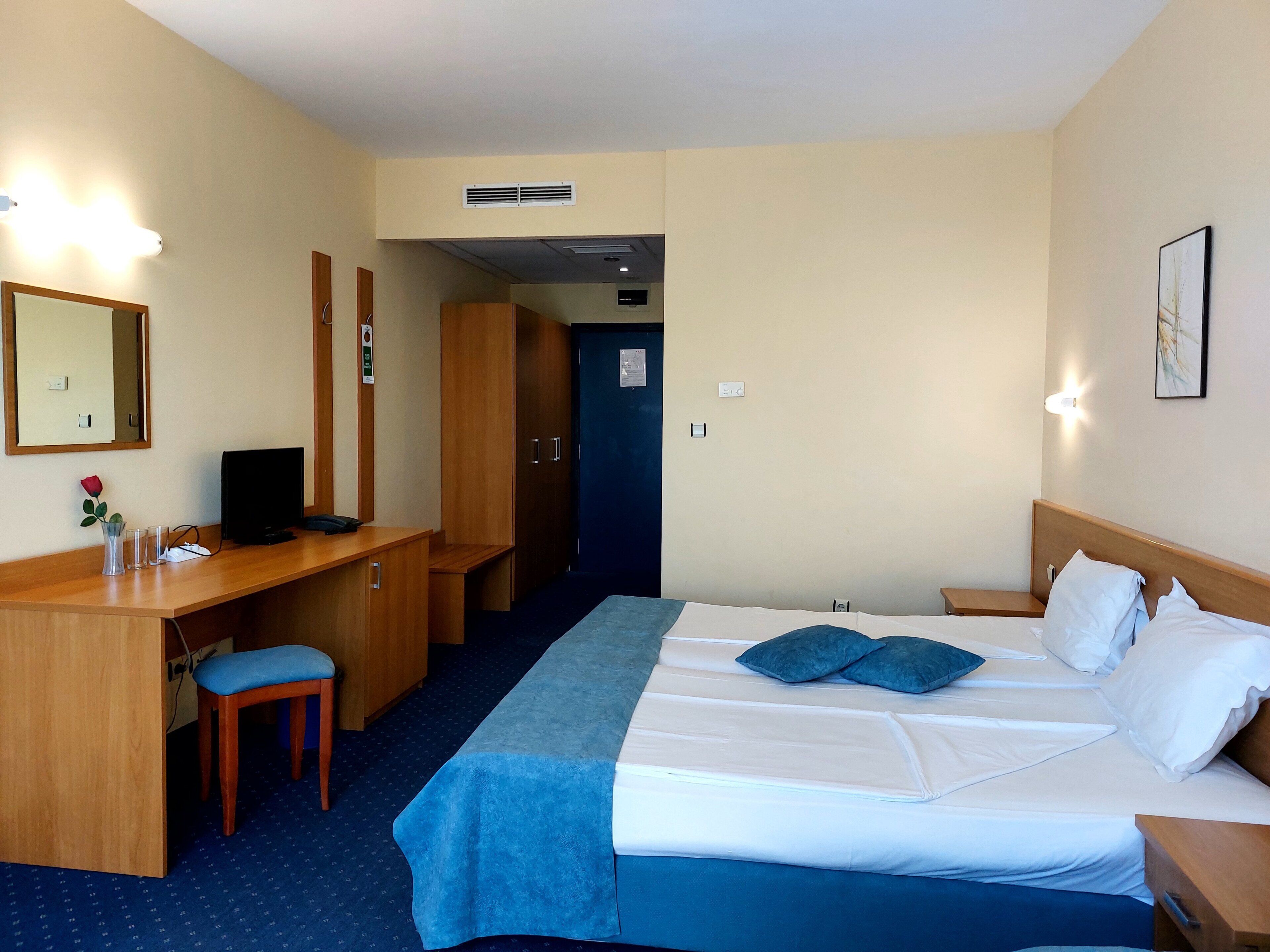 A hotel room with a bed, desk, chair, and a mirror.