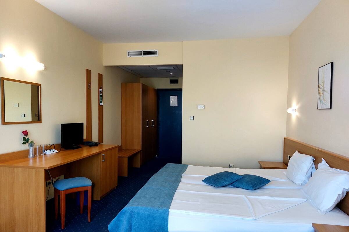A hotel room with a bed, desk, chair, and a mirror.