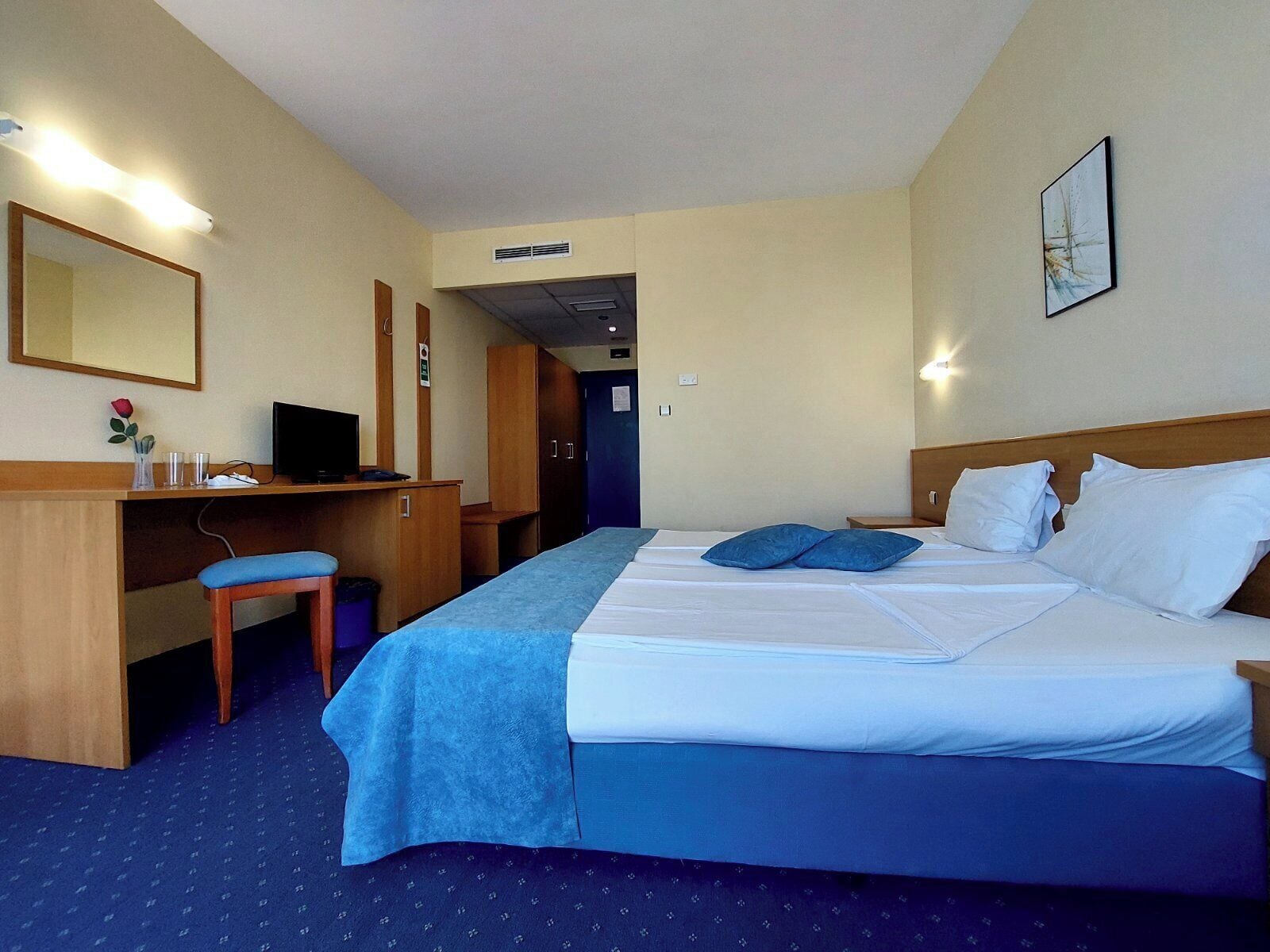 A hotel room with a bed, a desk, a chair, a television, and a mirror.