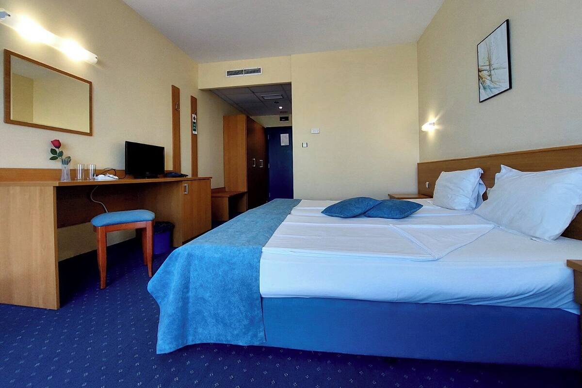 A hotel room with a bed, a desk, a chair, a television, and a mirror.