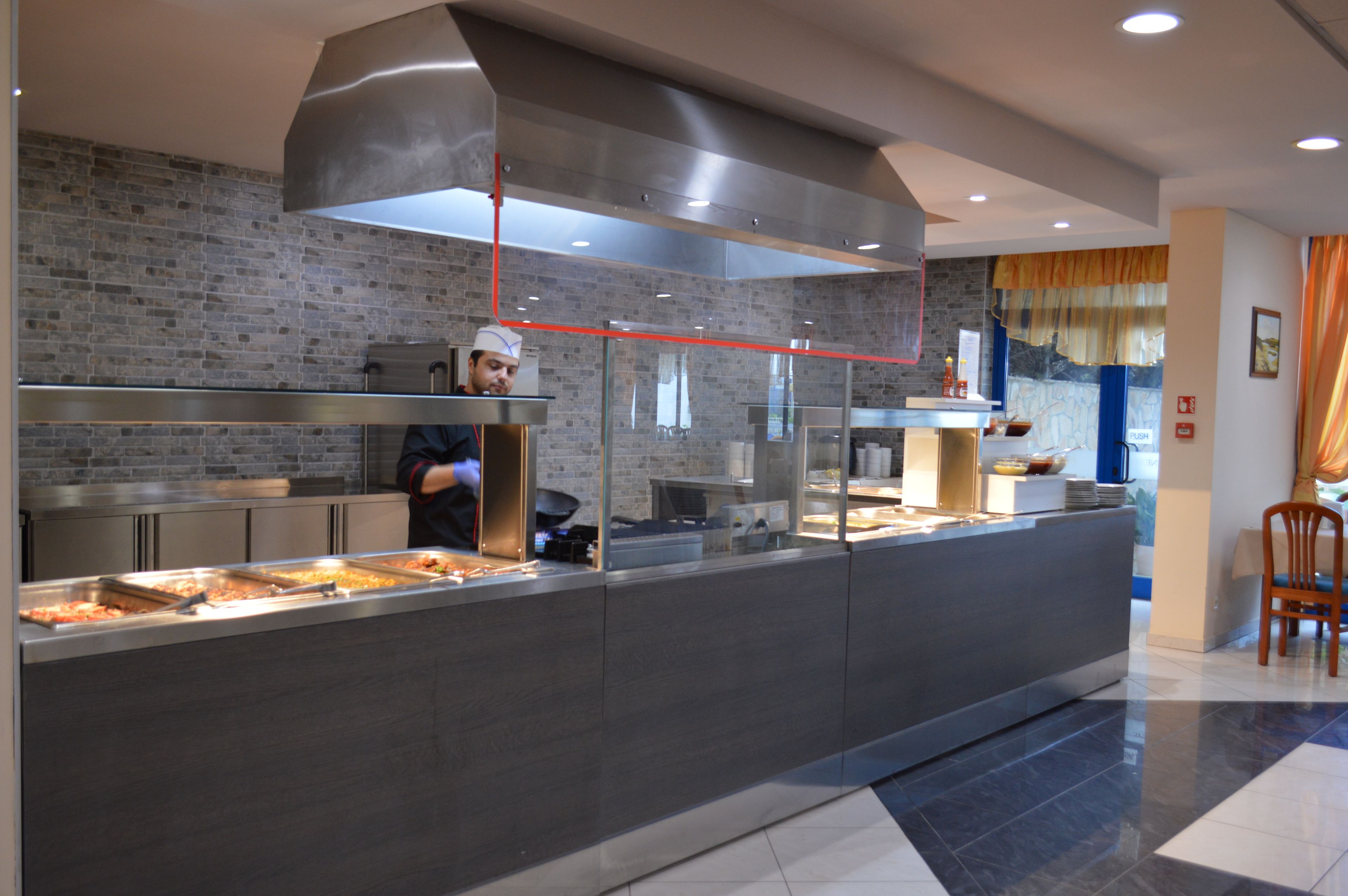 A modern kitchen area with a chef preparing food, a stainless steel counter, and a brick wall backdrop.