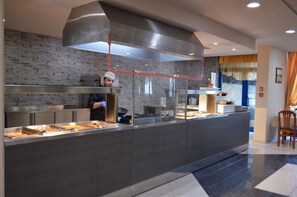 Un espace cuisine moderne où un chef prépare des plats, avec un comptoir en acier inoxydable et un mur en briques en arrière-plan.