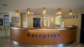 A reception desk with a 'Reception' sign, a bulletin board with notices, and a clock on the wall. - Aquamarine Hotel (Nessebar)