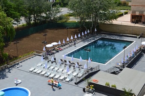 Un área de piscina en la azotea con sillones, sombrillas y una piscina.