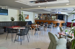 Un vestíbulo con zona de bar, disposición de asientos y una pantalla de televisión.