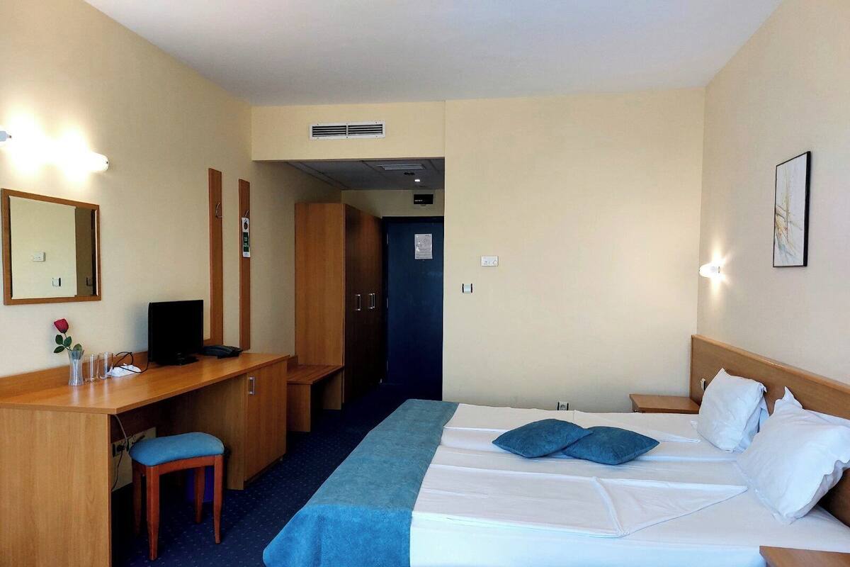 A hotel room with a bed, a desk, a chair, a mirror, and a door.