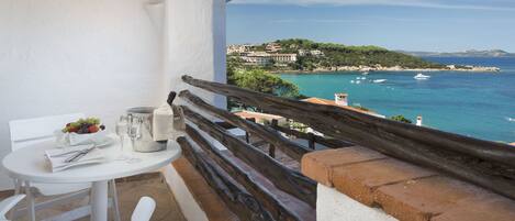 A balcony with a table set for dining, overlooking a coastal area with buildings and boats.
