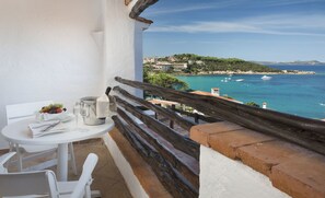 Un balcon avec une table dressée pour le dîner, donnant sur une zone côtière avec des bâtiments et des bateaux.