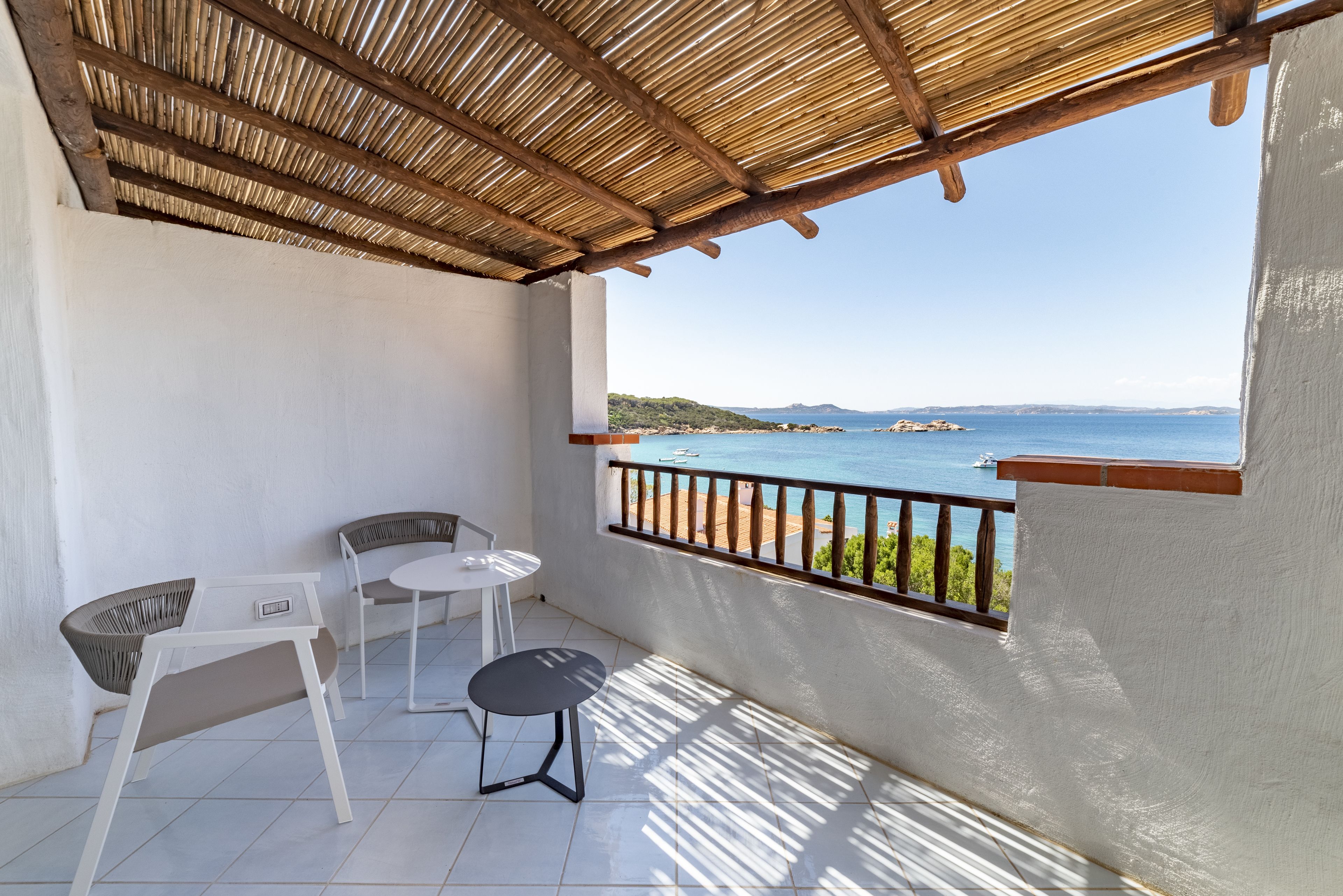 A balcony with a view of the sea, a table, and two chairs.