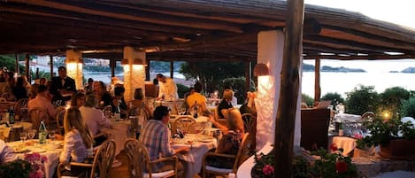 An outdoor dining area with tables and chairs, overlooking a body of water.