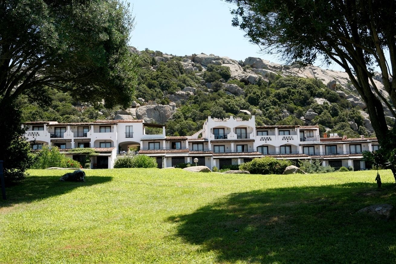 A hotel with multiple white buildings, balconies, and a mountainous backdrop.
