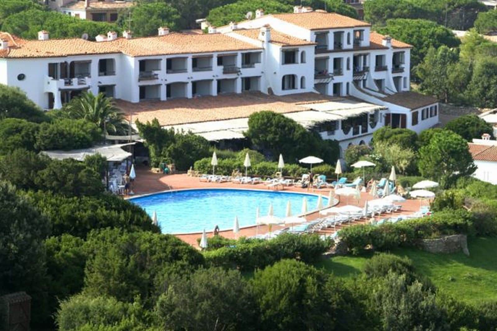 Ein großes, mehrstöckiges Gebäude mit einem Swimmingpool, umgeben von Liegestühlen und Sonnenschirmen.