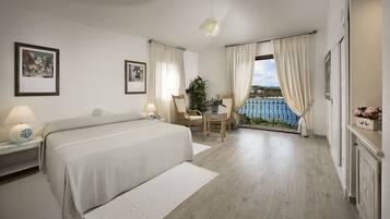 A hotel room with a bed, a chair, a table, and a view of the sea.