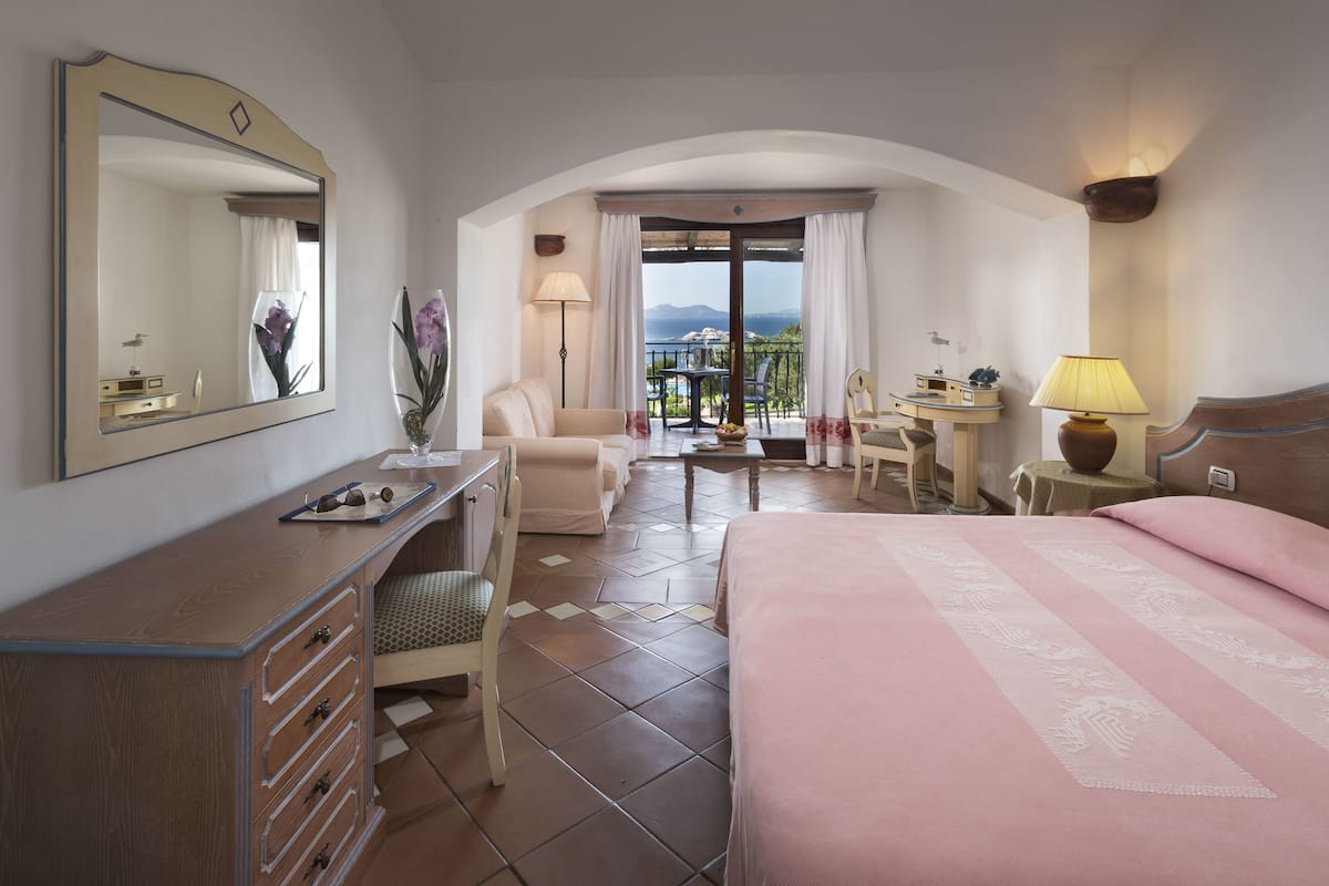 Habitación de hotel con cama, escritorio, silla, una mesita y vistas al exterior.