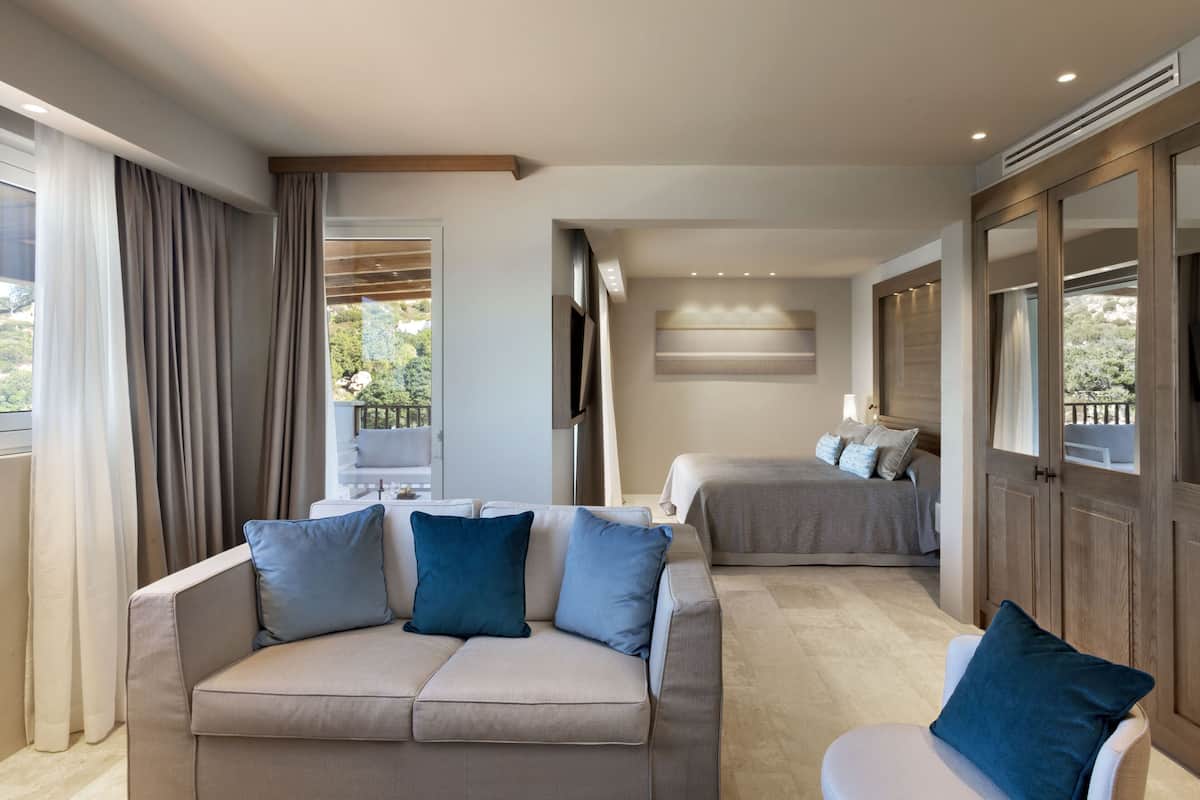 Una habitación de hotel moderna con sofá, sillón, cama y un gran ventanal.