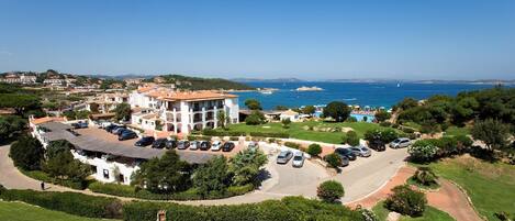 A coastal hotel with a large building, a parking lot, and a view of the sea.